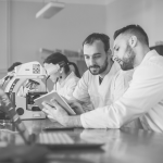 A group of people in lab coats looking at a tablet